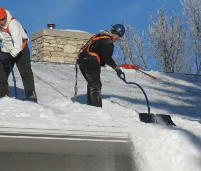 Professional technicians performing roof snow removal with safety harnesses and shovels in Nashville, TN